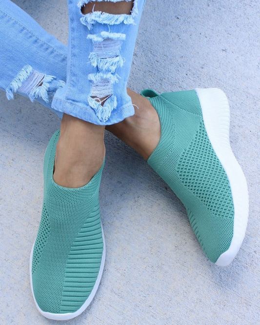 Schwarze Slip-On-Sneaker aus atmungsaktivem Strickmaterial, kombiniert mit zerrissenen Jeans. Bequeme Freizeitschuhe für Damen.
