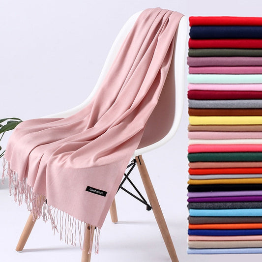 Eleganter rosa Schal aus Kaschmir, drapiert auf einem Stuhl, mit einer Auswahl an bunten Stoffen im Hintergrund. Weicher, luxuriöser Schal für Damen.